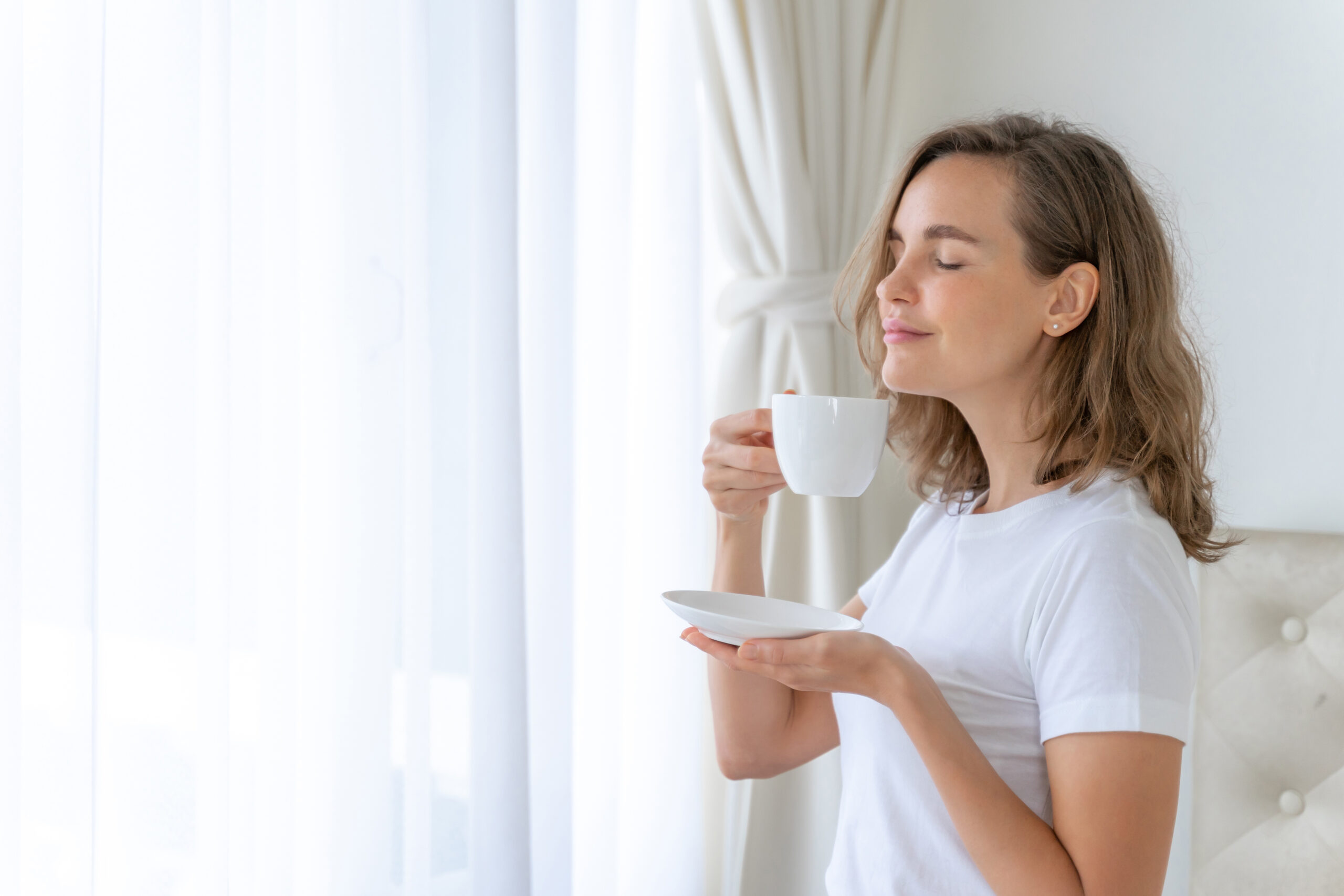 Beautiful beauty woman cute girl feel happy drinking coffee in the morning , enjoying time in her home  white bedroom background - lifestyle beauty woman concept